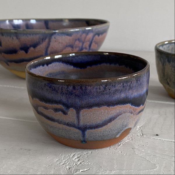 Three handmade ceramic bowls with a glossy glaze featuring blue, purple, and pink marbled patterns, displayed on a light gray surface.