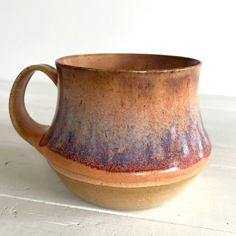 Ceramic mug with brown and purple glaze on a white surface