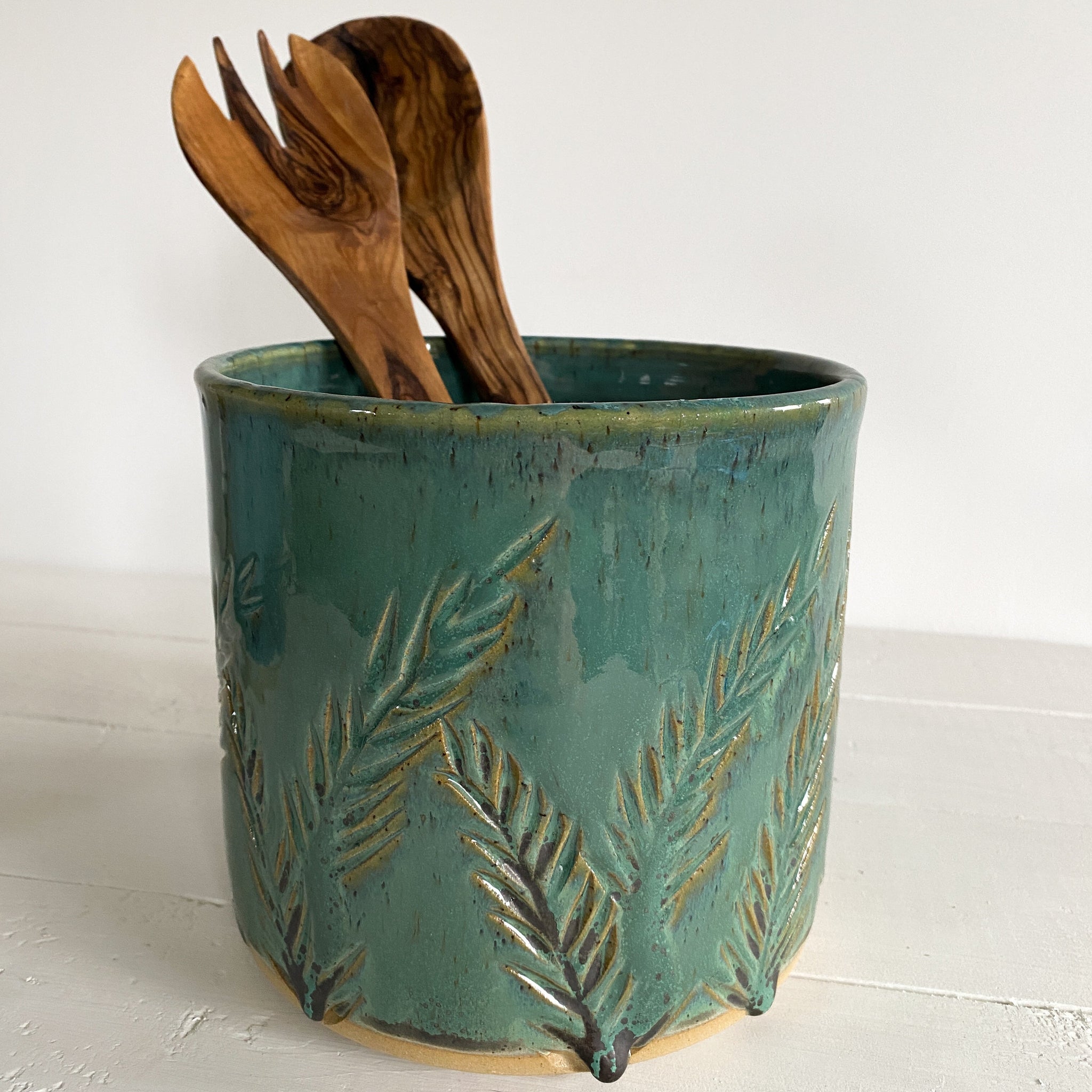 Teal ceramic utensil holder with wooden utensils on a white background