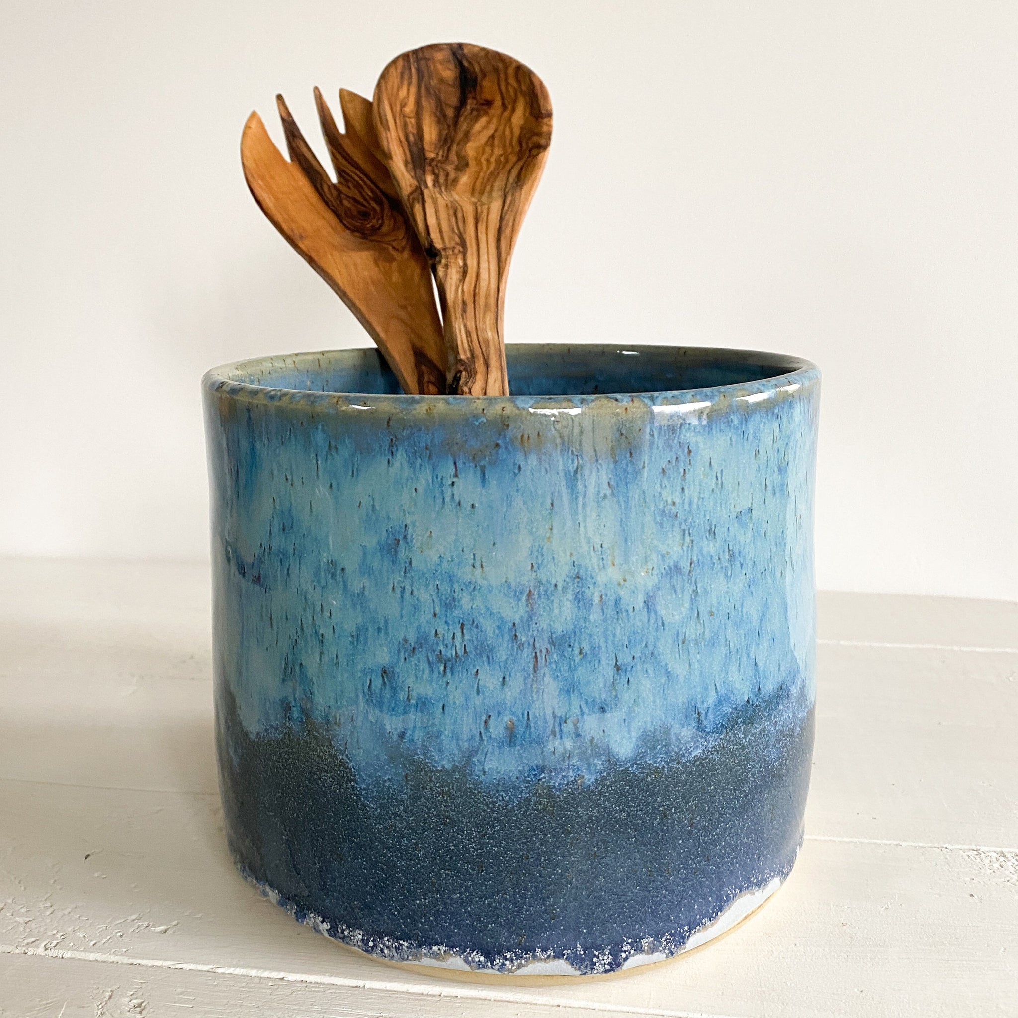 Blue ceramic container with wooden utensils on a white surface