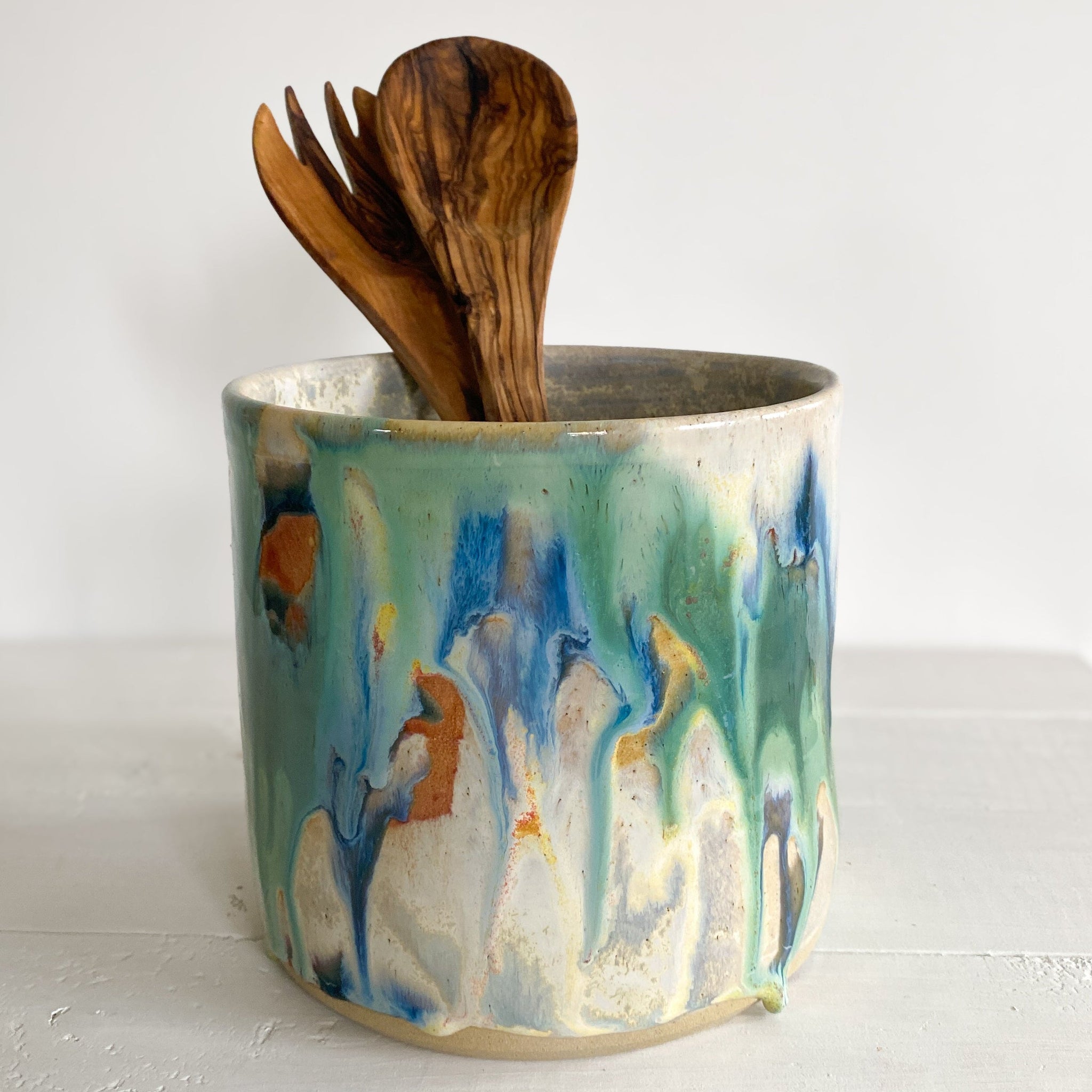 Utensil holder with abstract design holding wooden utensils on a white surface.