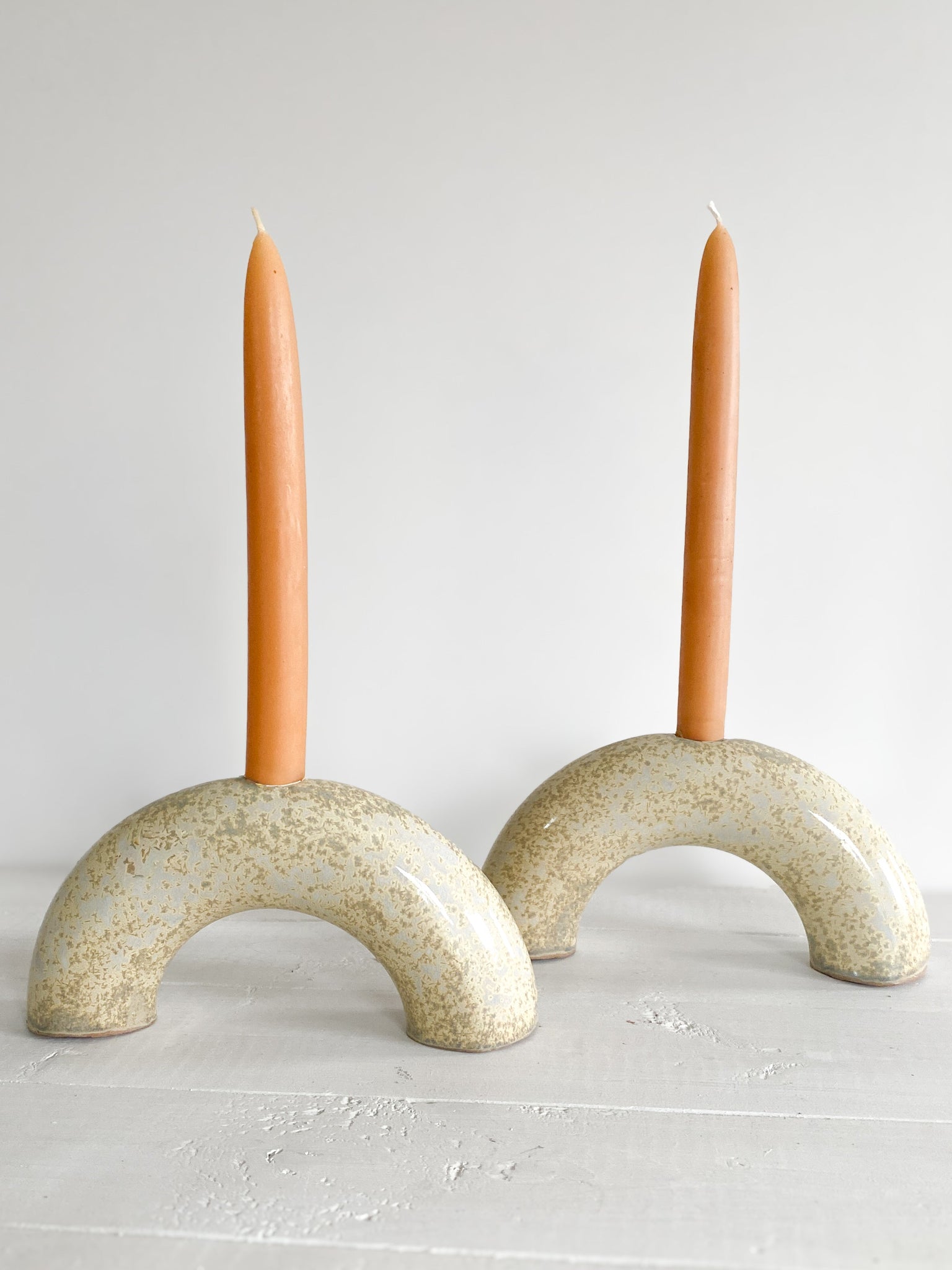 Two ceramic arch-shaped candle holders with two candles on a light gray background