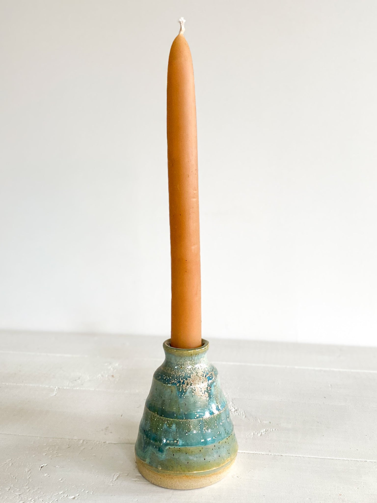 Candle in a teal ceramic holder on a white surface