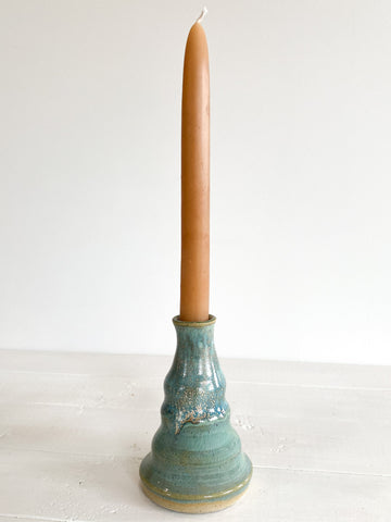 Turquoise ceramic candle holder with a beige candle on a white surface