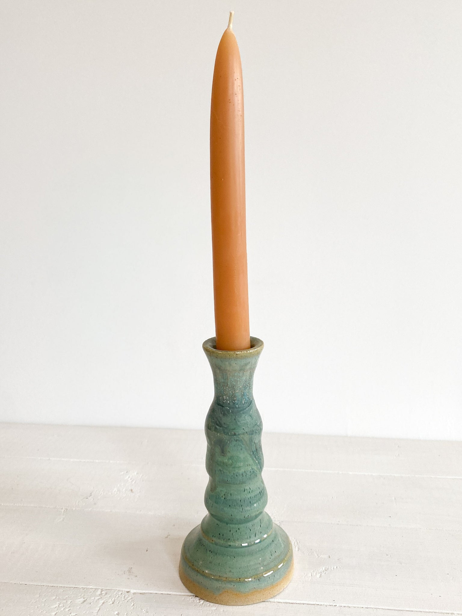Green ceramic candle holder with a candle on a white surface