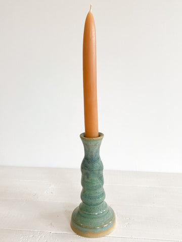 Green ceramic candle holder with a candle on a white surface