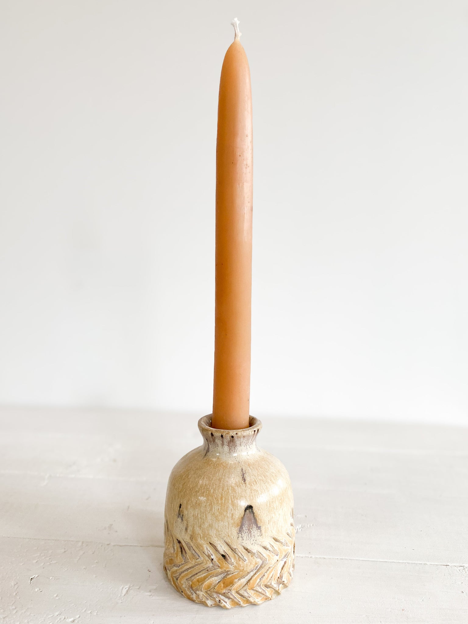 Ceramic candle holder with a brown candle on a white surface