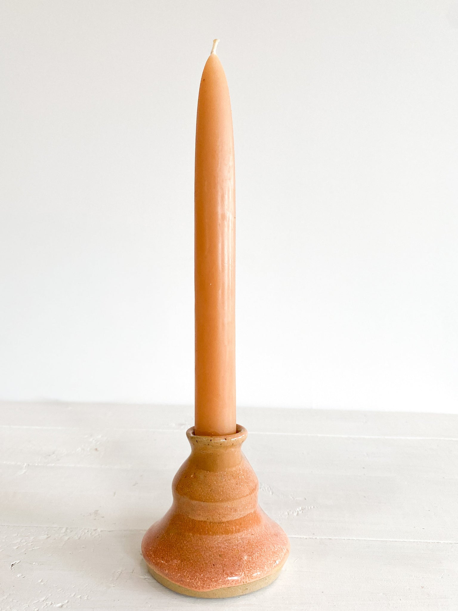 Tall candle in a terracotta-colored ceramic holder on a white surface