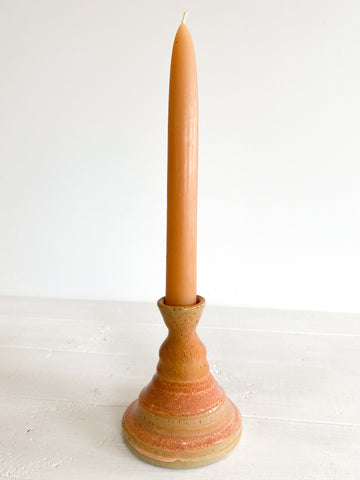 Tall, thin candle in a terracotta holder on a white surface