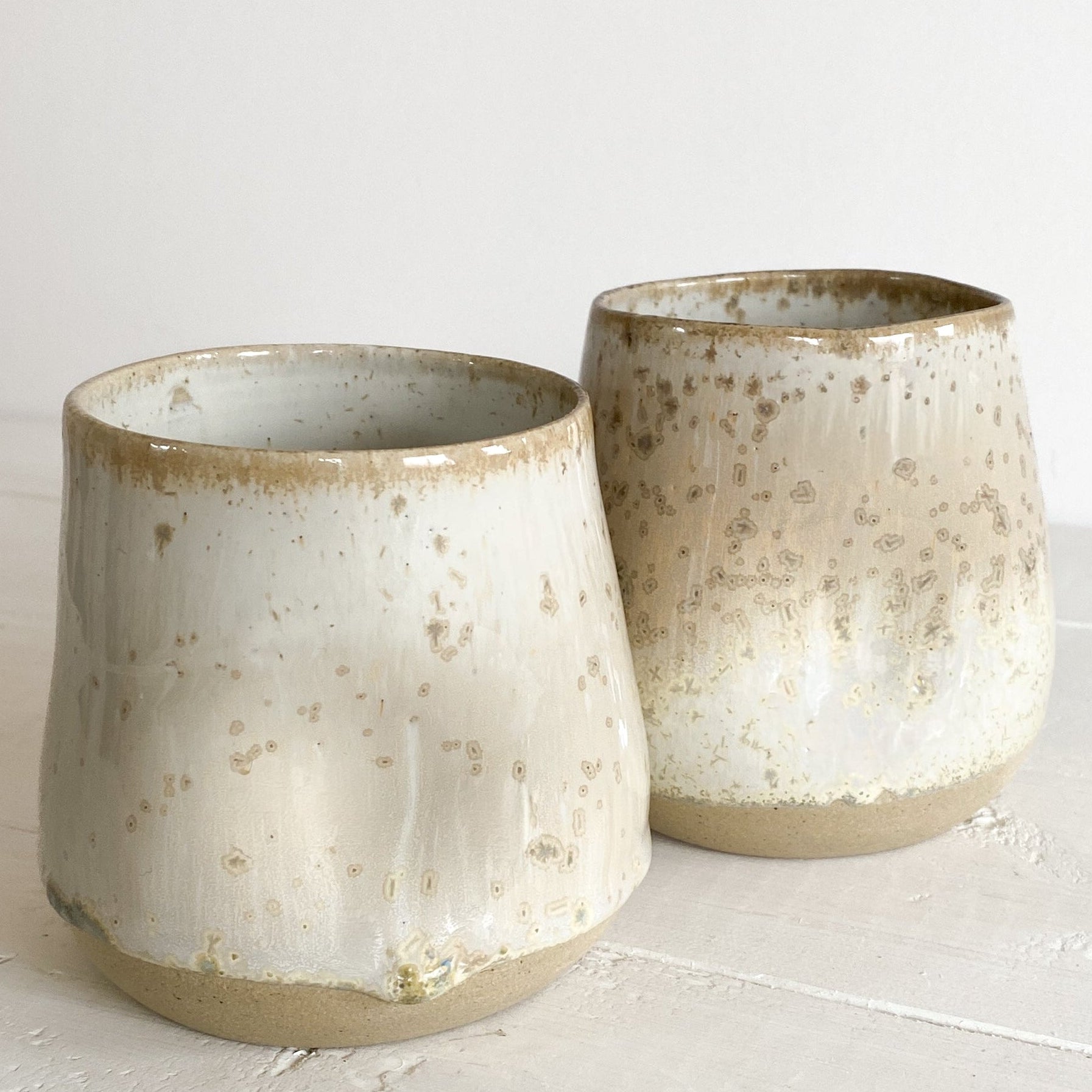 Two ceramic pots with speckled glaze on a light surface