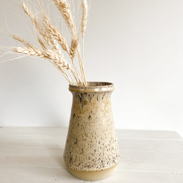 Speckled ceramic vase with dried wheat on a white wooden surface