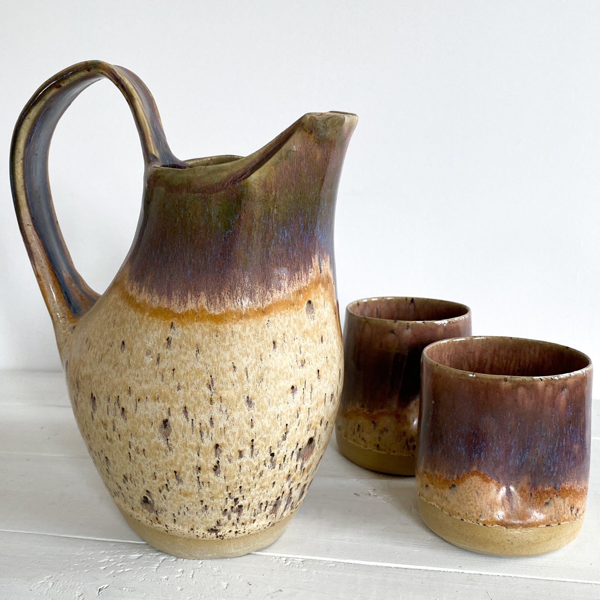 Stoneware pitcher and two cups on a white surface with a white background
