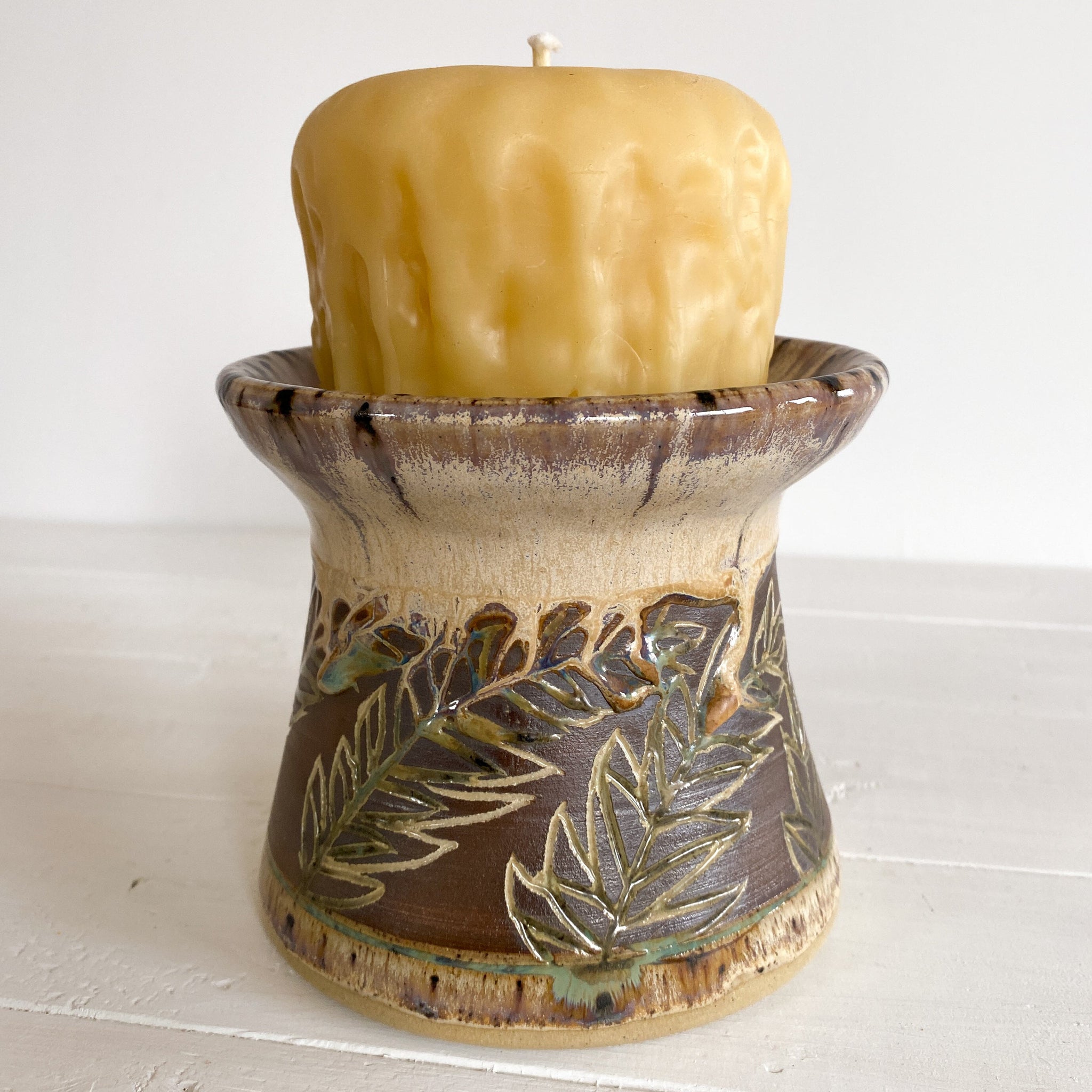 Ceramic candle holder with leaf patterns holding a candle on a white surface