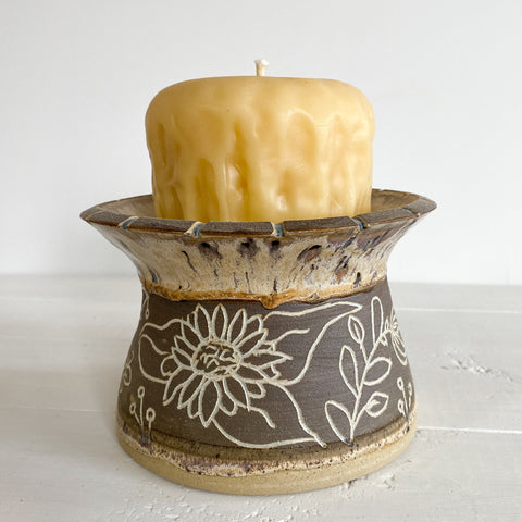 Ceramic candle holder with a floral design holding a candle on a white surface.