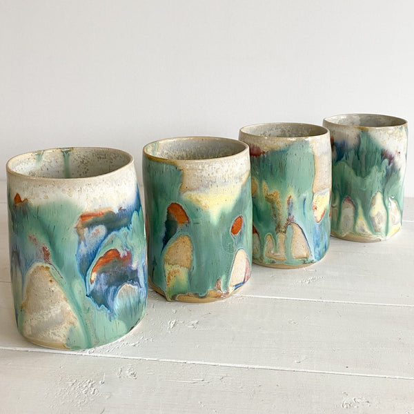Four ceramic cups with abstract green and blue glaze on a white surface.