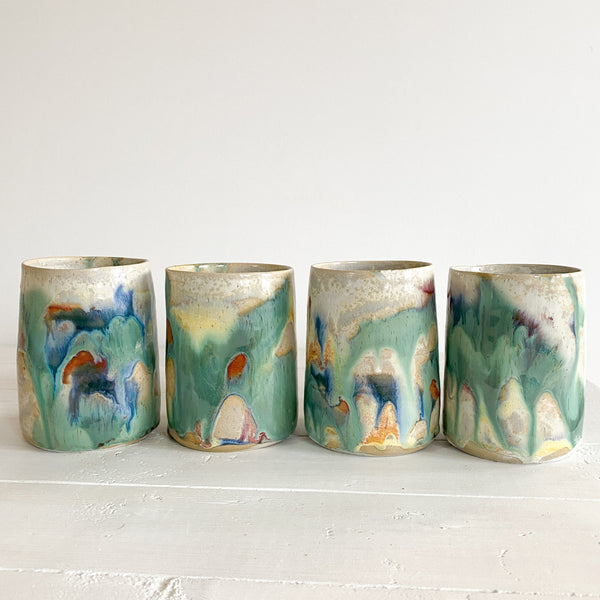 Four ceramic cups with abstract multicolor designs on a white surface.
