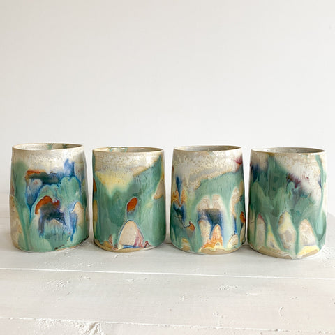 Four ceramic cups with abstract multicolor designs on a white surface.