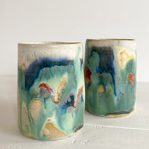 Two ceramic tumblers with abstract multicolor glaze on a white surface.