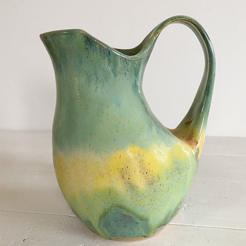 Green and yellow ceramic pitcher on a white surface with a white background