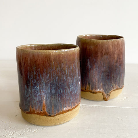 Two purple brown ceramic cups on a light gray surface with a white background