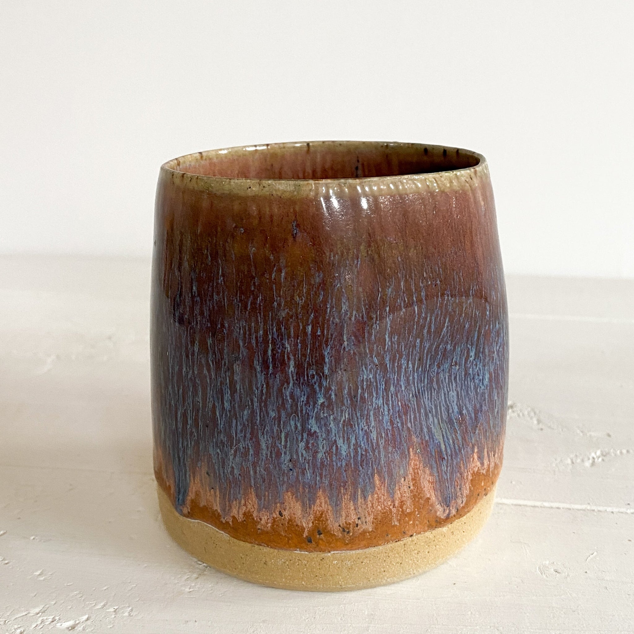 Ceramic cup with brown and purple glaze on a white background