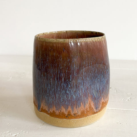 Ceramic cup with brown and purple glaze on a white background