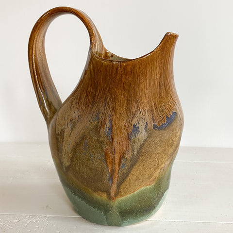 Ceramic pitcher with brown and green glaze on a white surface