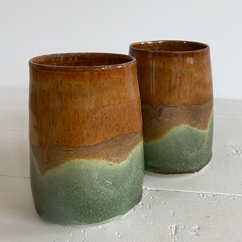 Two ceramic tumblers with a two-tone brown and green glaze on a light gray surface.