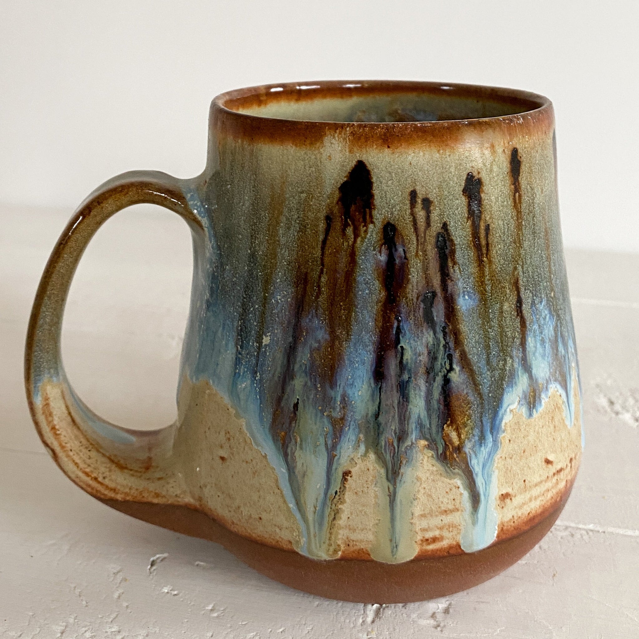 Handmade ceramic mug with a multicolored glaze on a light wooden surface.