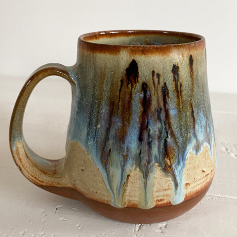 Handmade ceramic mug with a multicolored glaze on a light wooden surface.