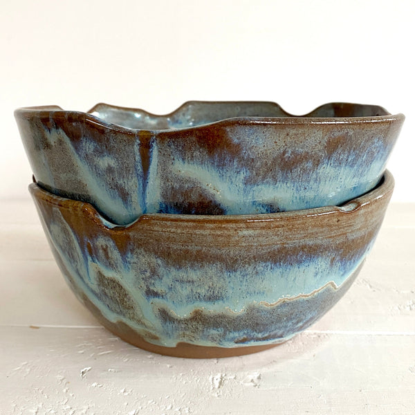 Two ceramic bowls with a textured blue and brown glaze on a light background