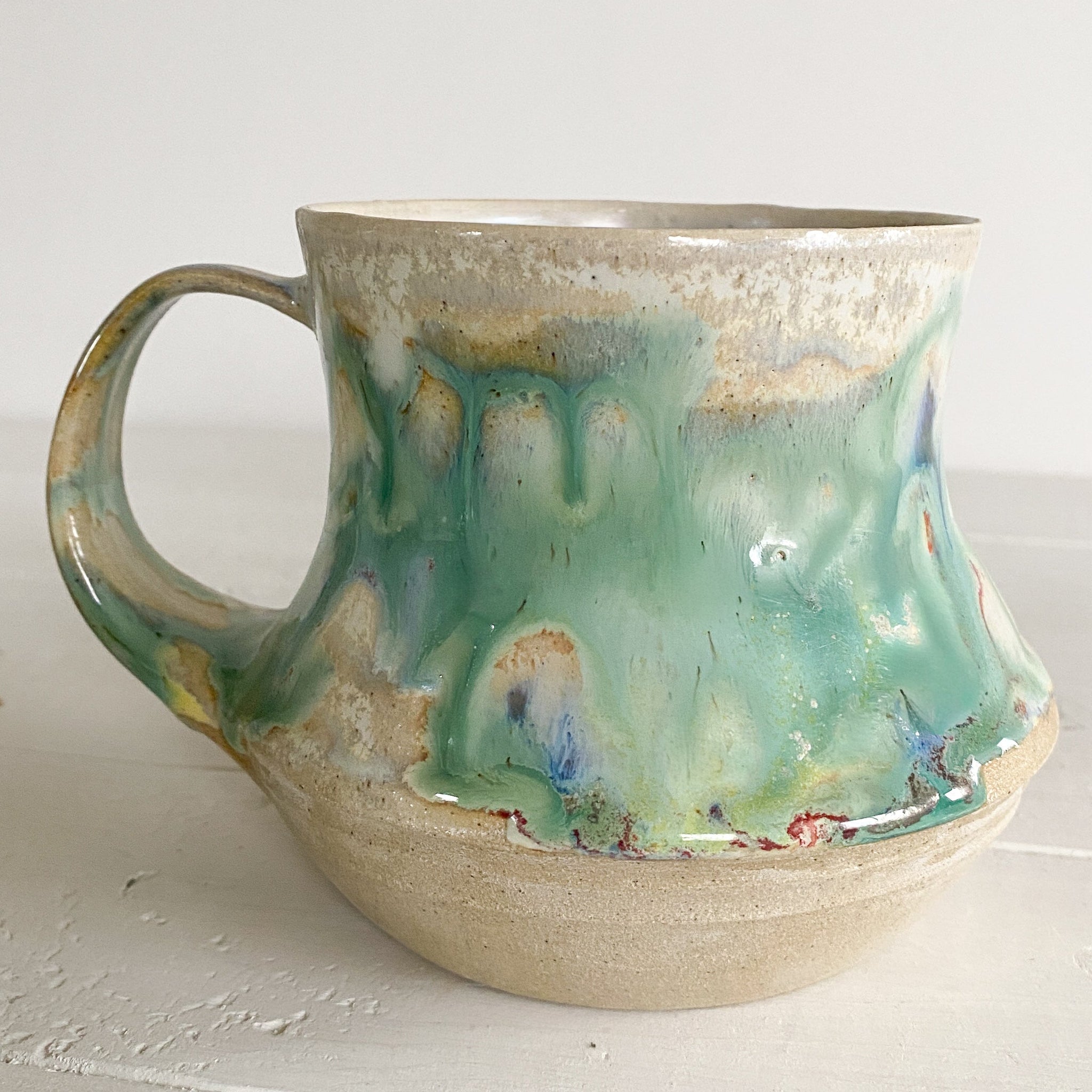 Handmade ceramic mug with green and beige glaze on a white surface