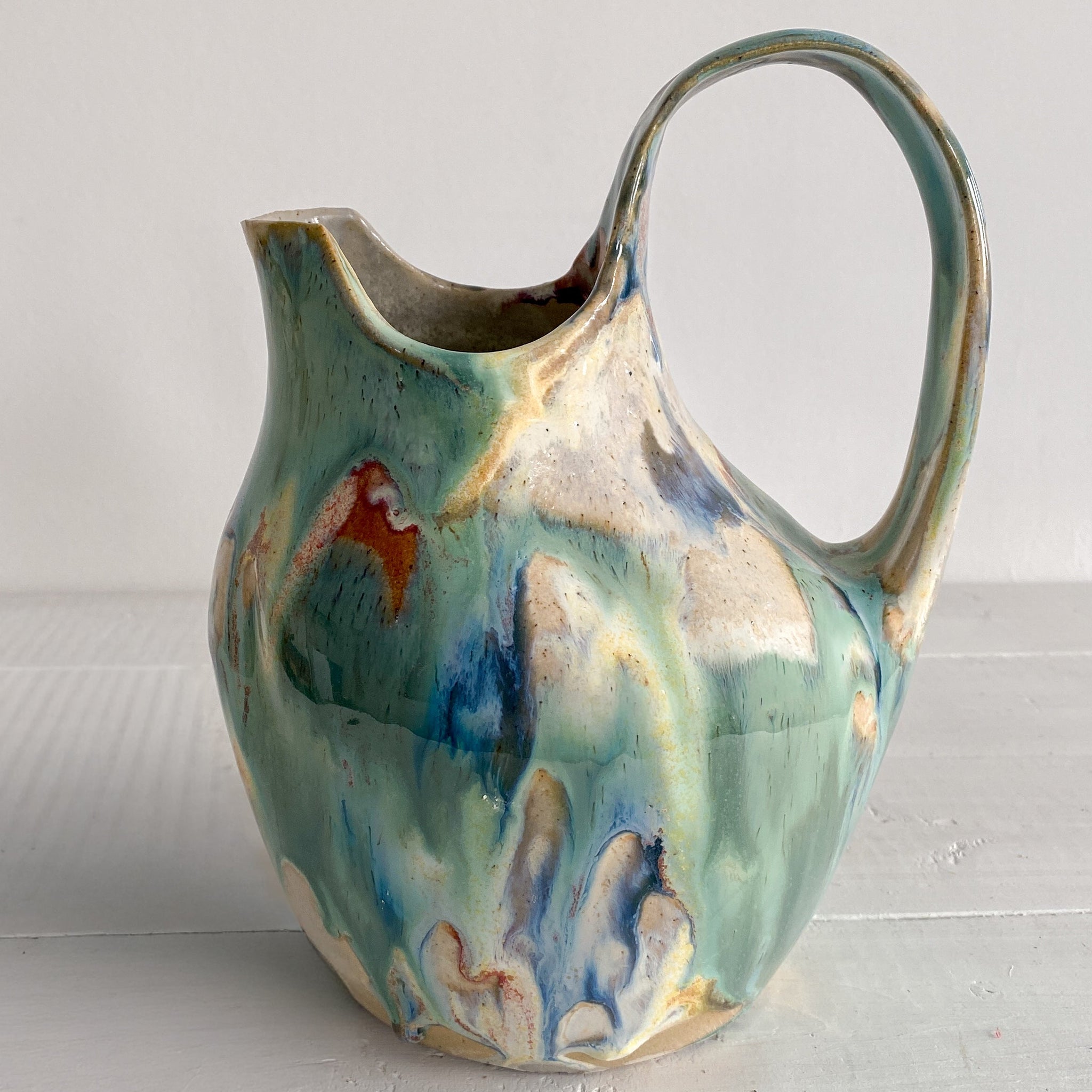 Decorative ceramic pitcher with multicolored glaze on a light gray surface.