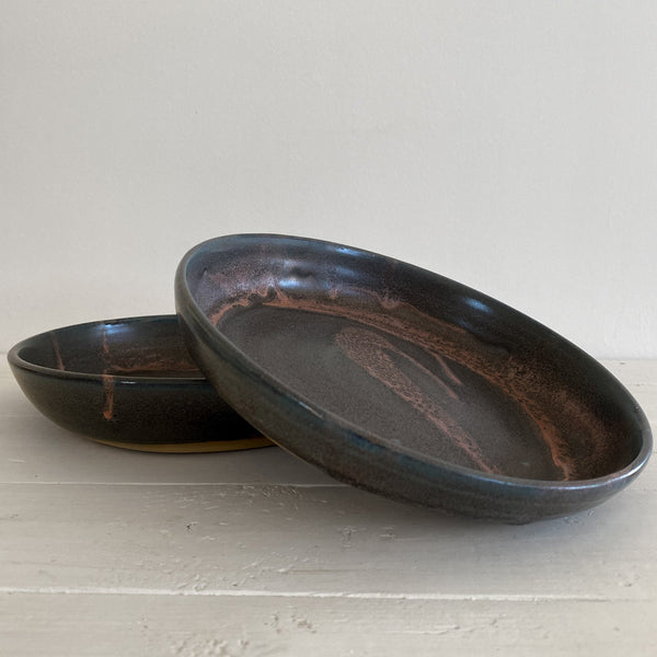 Two black ceramic plates on a light gray surface with a white background