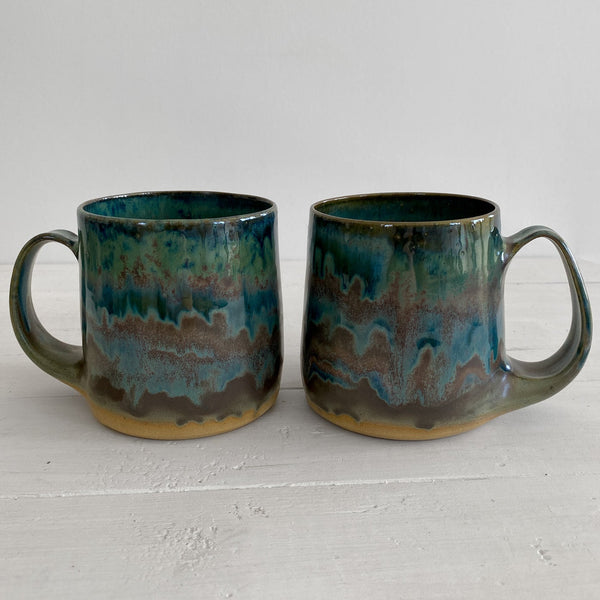 Two ceramic mugs with a textured green and brown glaze on a light gray background