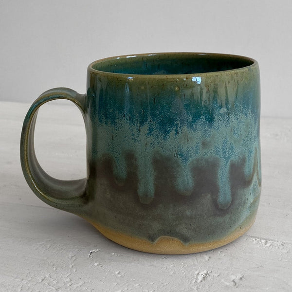 Green ceramic mug on a light gray surface with a neutral background