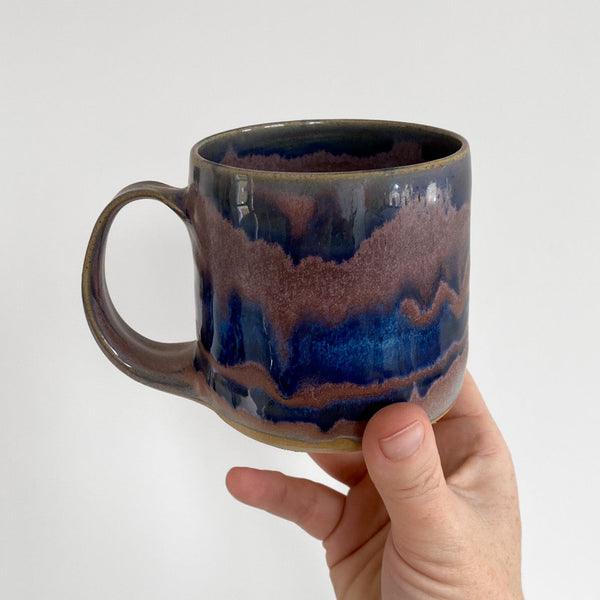 Hand holding a ceramic mug with blue and brown glaze on a white background