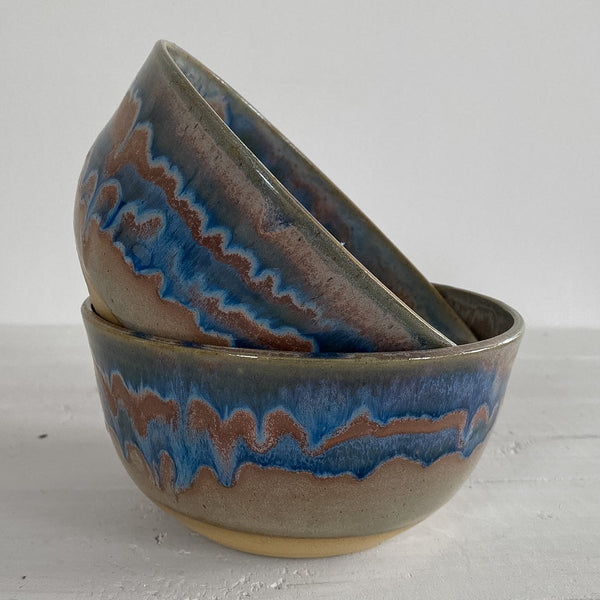 Two ceramic bowls with blue and brown glaze on a light gray surface.