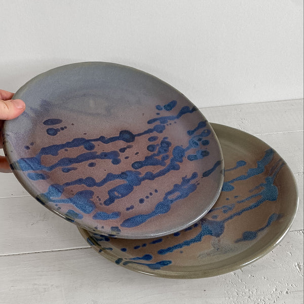 Hand holding a ceramic plate with blue abstract design on a light wooden surface