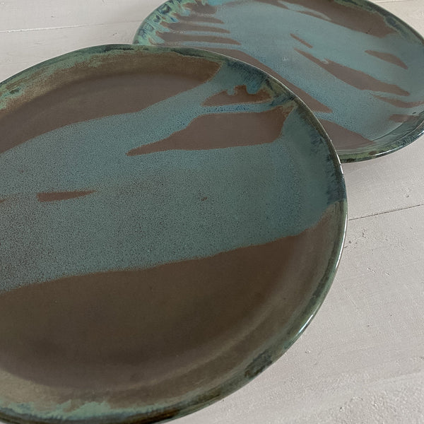 Two ceramic plates with a green and brown glaze on a light gray surface.