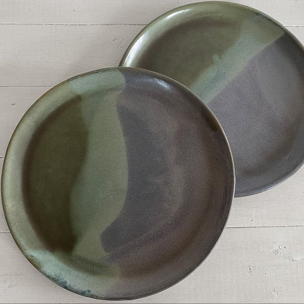 Two ceramic plates with a green and brown glaze on a light wooden surface.